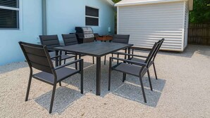 Een terras met een tafel, stoelen, een barbecue en een tuinhuis.