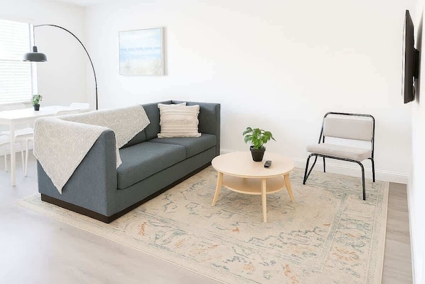 Una sala de estar moderna con un sofá gris, una mesita redonda, una pequeña planta en maceta y una silla blanca.