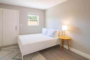 Un dormitorio con cama, una mesita de noche con lámpara, una ventana y una puerta.