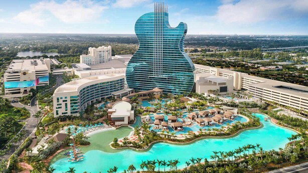 Ein Resort mit einem gitarrenförmigen Gebäude, mehreren Schwimmbecken und üppiger Bepflanzung.