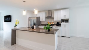 Una cocina moderna con armarios blancos, una isla central, electrodomésticos de acero inoxidable e iluminación colgante.