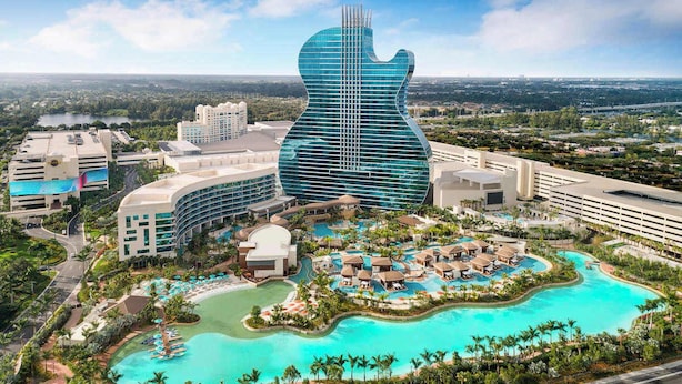 Un resort con un edificio en forma de guitarra, varias piscinas y abundante vegetación.