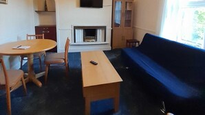 A living room with a sofa, a dining table with chairs, a fireplace, a television mounted on the wall, and a window with curtains. - A 2 bed flat in clentral Dumfries, excellent walkability to all amenities. (Dumfries)