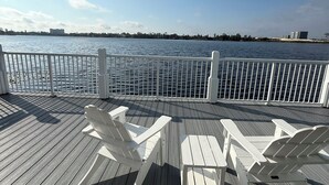 Eine Holzterrasse mit weißen Stühlen und einem Geländer, das auf ein Gewässer blickt.