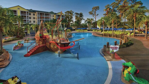 Ein großer Pool mit einem Piratenschiff-Spielbereich, Liegestühlen und Palmen.