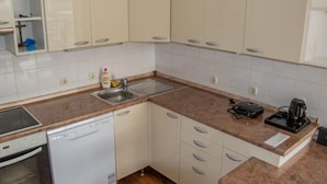 A compact kitchen with white cabinets, a dishwasher, a sink, and a coffee maker. - Apartments Rivijera 1 (Crikvenica)