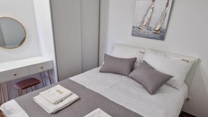 A neatly made bed with a gray and white color scheme, a small bedside table, and a wall-mounted mirror. - Apartments Rivijera 1 (Crikvenica)