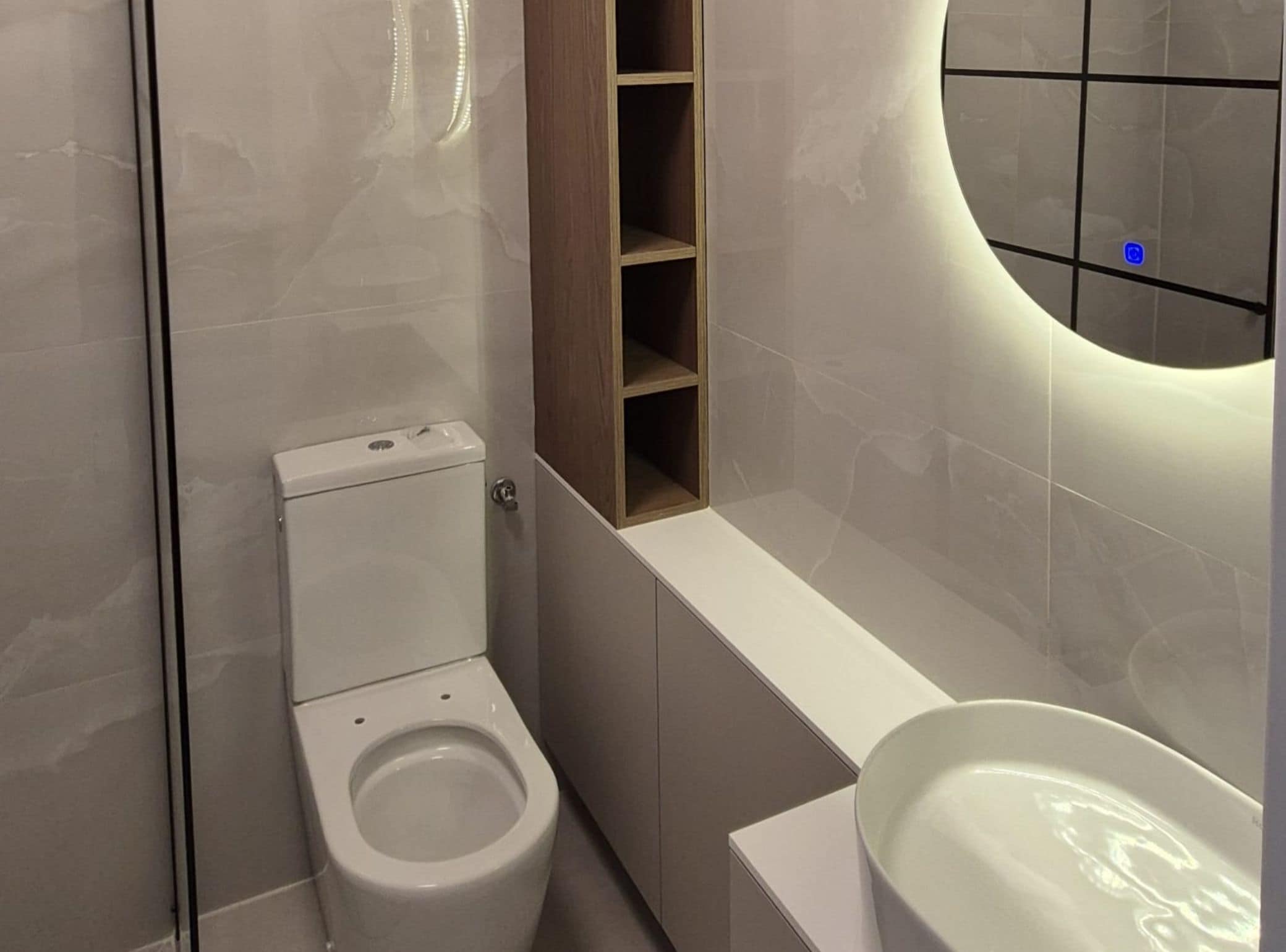 Un baño moderno con inodoro, estante empotrado y tocador con espejo.
