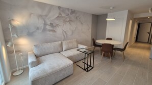 A modern living room with a sectional sofa, a glass coffee table, and a dining area with a round table and chairs. - Apartments Rivijera 2 (Crikvenica)