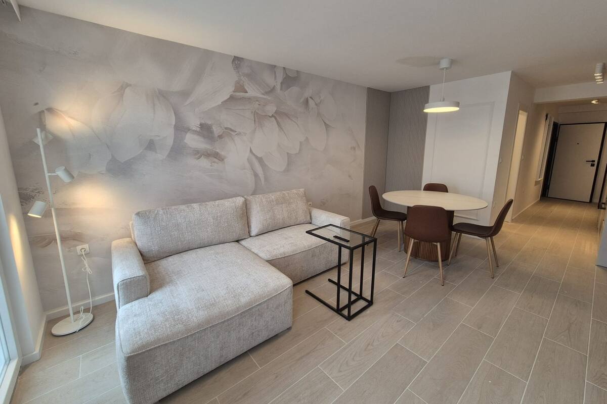 Un salon moderne avec un canapé d’angle, une table basse en verre et un coin repas comprenant une table ronde et des chaises.