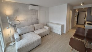 A modern living room with a sectional sofa, a white cabinet, and a dining area with brown chairs. - Apartments Rivijera 2 (Crikvenica)