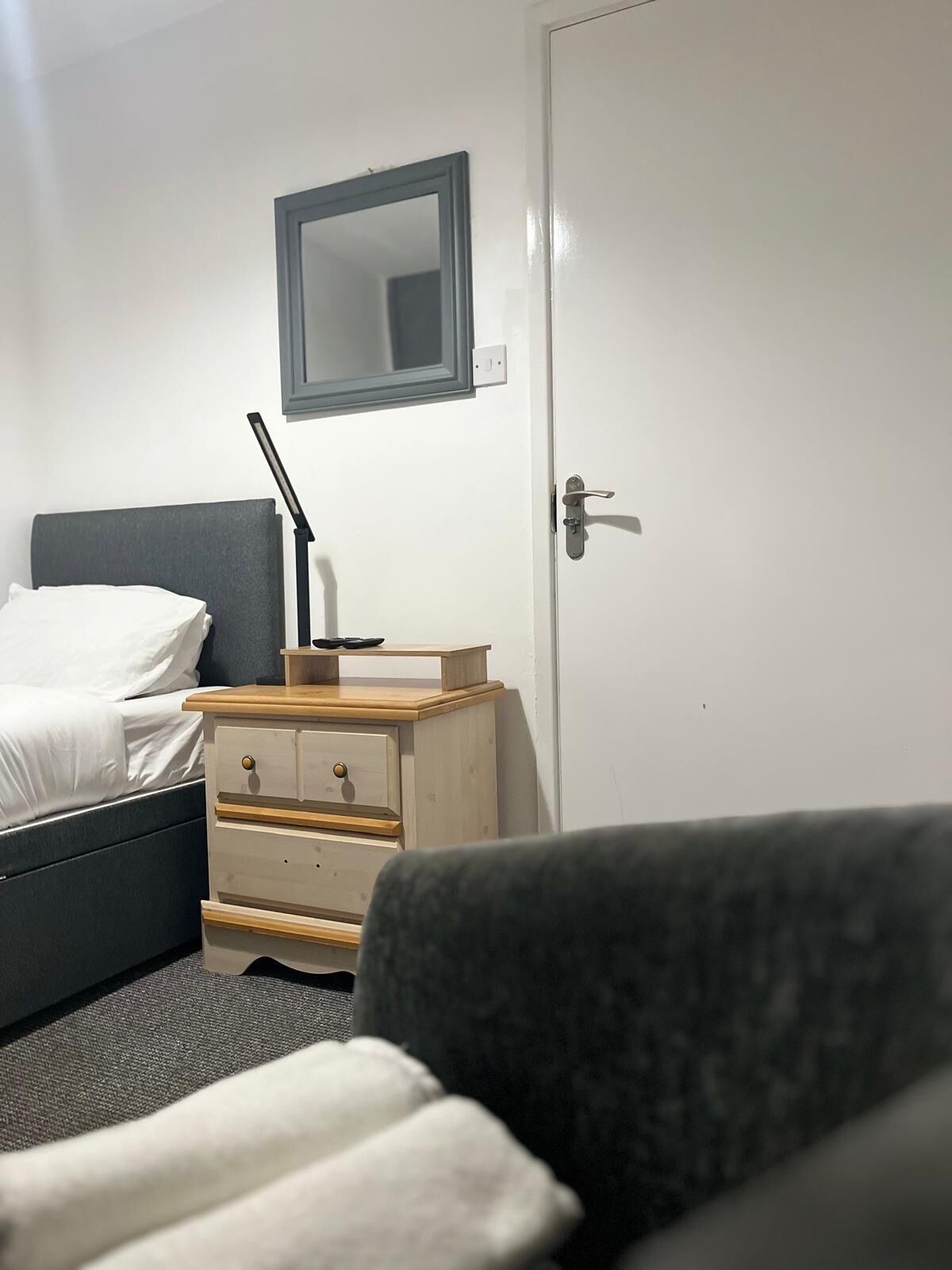 Ein Schlafzimmer mit einem Bett, einem Nachttisch mit Lampe, einer Kommode und einer Tür.