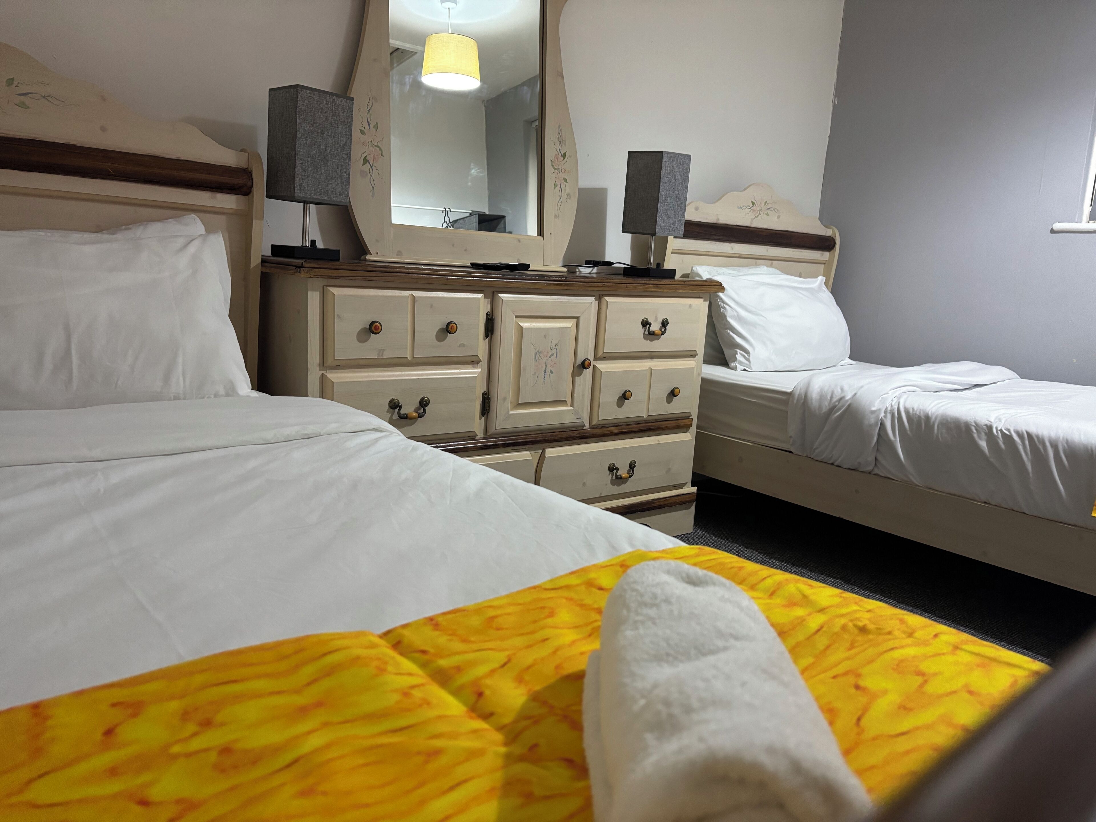 A hotel room with two beds, a dresser with drawers, a mirror, and a lamp.
