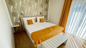 Una cama bien hecha con colcha blanca y naranja, suelo de madera y papel tapiz estampado con motivos florales.