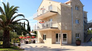 Un edificio de dos pisos con balcones, un área de estar al aire libre techada y una palmera.