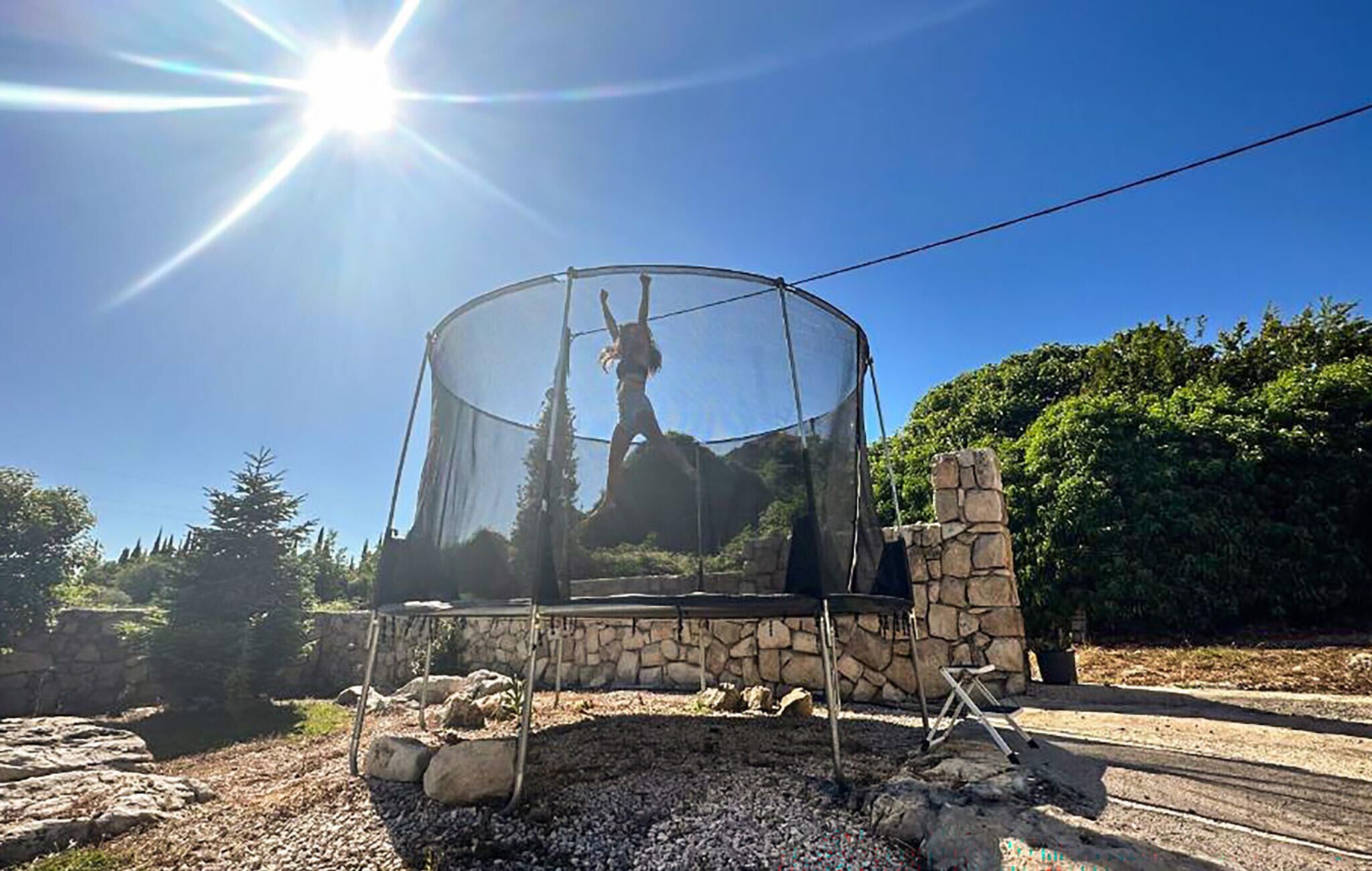 Cielo despejado con el sol brillando, una estructura de piedra con cerramiento de vidrio y un muro de piedra al fondo.