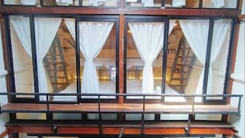 Interior de hotel com vários níveis, corrimão de varanda em madeira e cortinas brancas nas janelas.