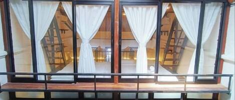A multi-level hotel interior with a wooden balcony railing and white curtains on the windows.