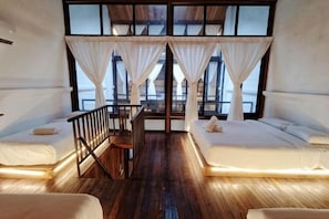 Een kamer met twee bedden, een houten vloer en uitzicht door grote ramen.