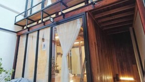A room with a wooden ceiling, a large window with sheer curtains, and a visible door leading to another room. - Ruma Papanz Moden 3Br 19 Pax by Jeffery Lam Home Management (Melaka)