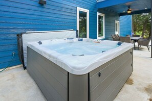 A hot tub in a covered outdoor area with a blue house in the background. - Modern Country Escape w/ Hot Tub & Total Privacy (Dale)