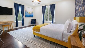 Ein Schlafzimmer mit Bett, Schreibtisch, Stuhl, Deckenventilator und einem großen Fenster mit Vorhängen.