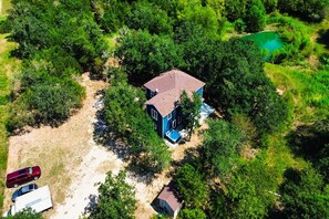 An aerial view of a house surrounded by dense greenery, with a small pond nearby. - Modern Country Escape w/ Hot Tub & Total Privacy (Dale)