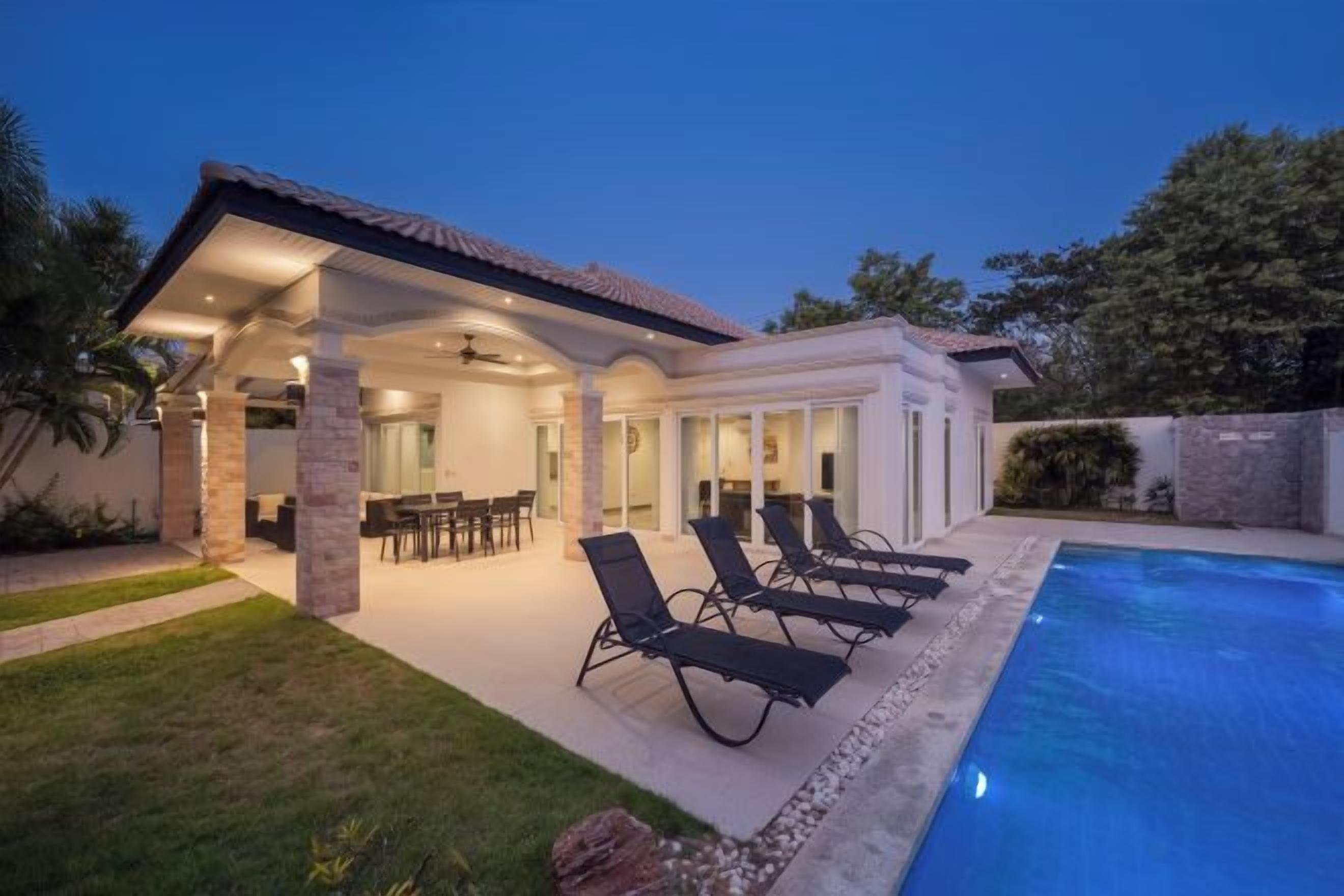 Un área junto a la piscina con sillones de descanso, un porche cubierto y una piscina.