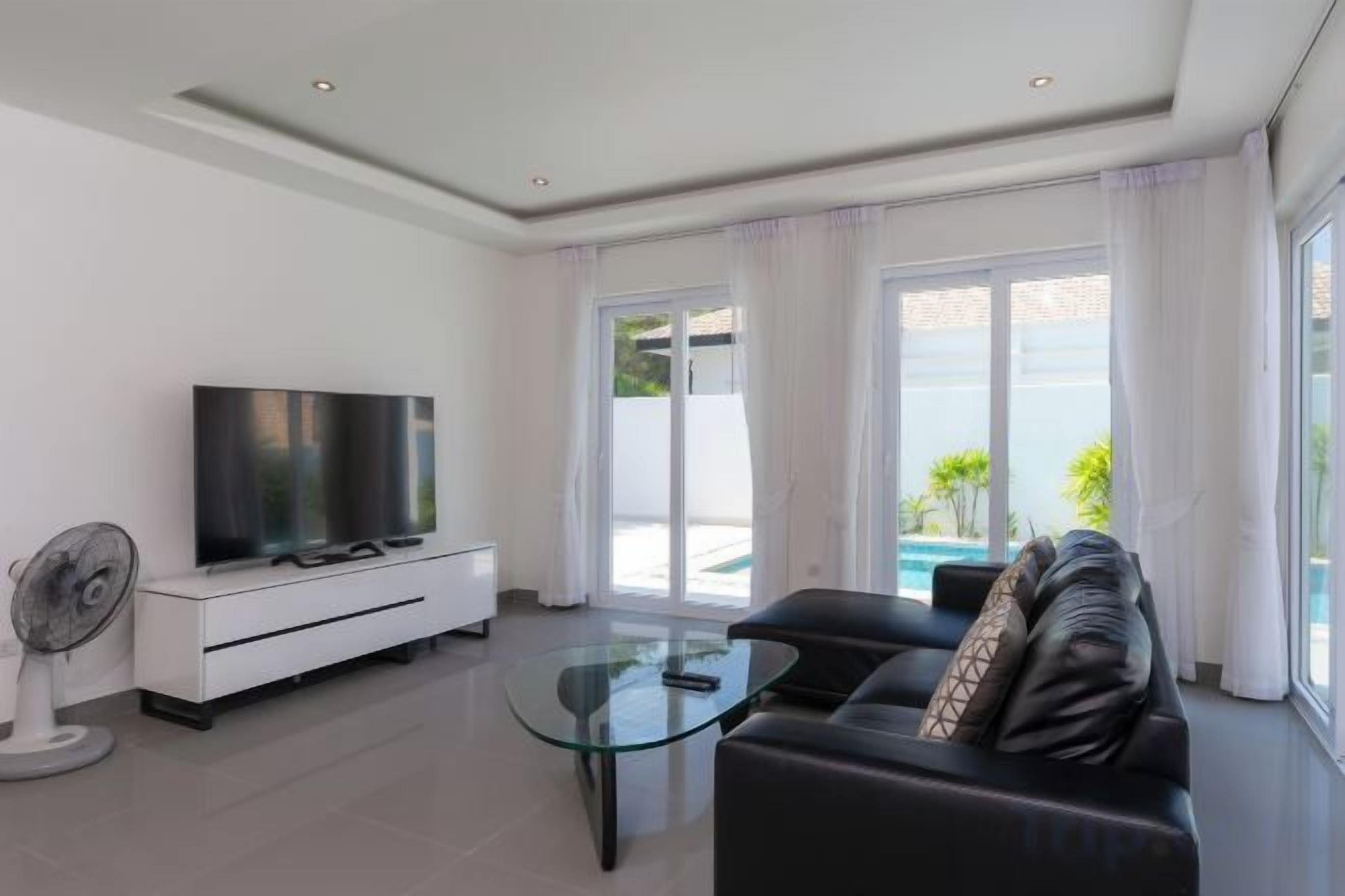 Een moderne woonkamer met een flatscreen televisie, een glazen salontafel, een bank en een ventilator.