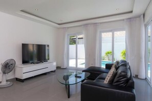 Ein modernes Wohnzimmer mit einem Flachbildfernseher, einem Glastisch, einer Couch und einem Ventilator.