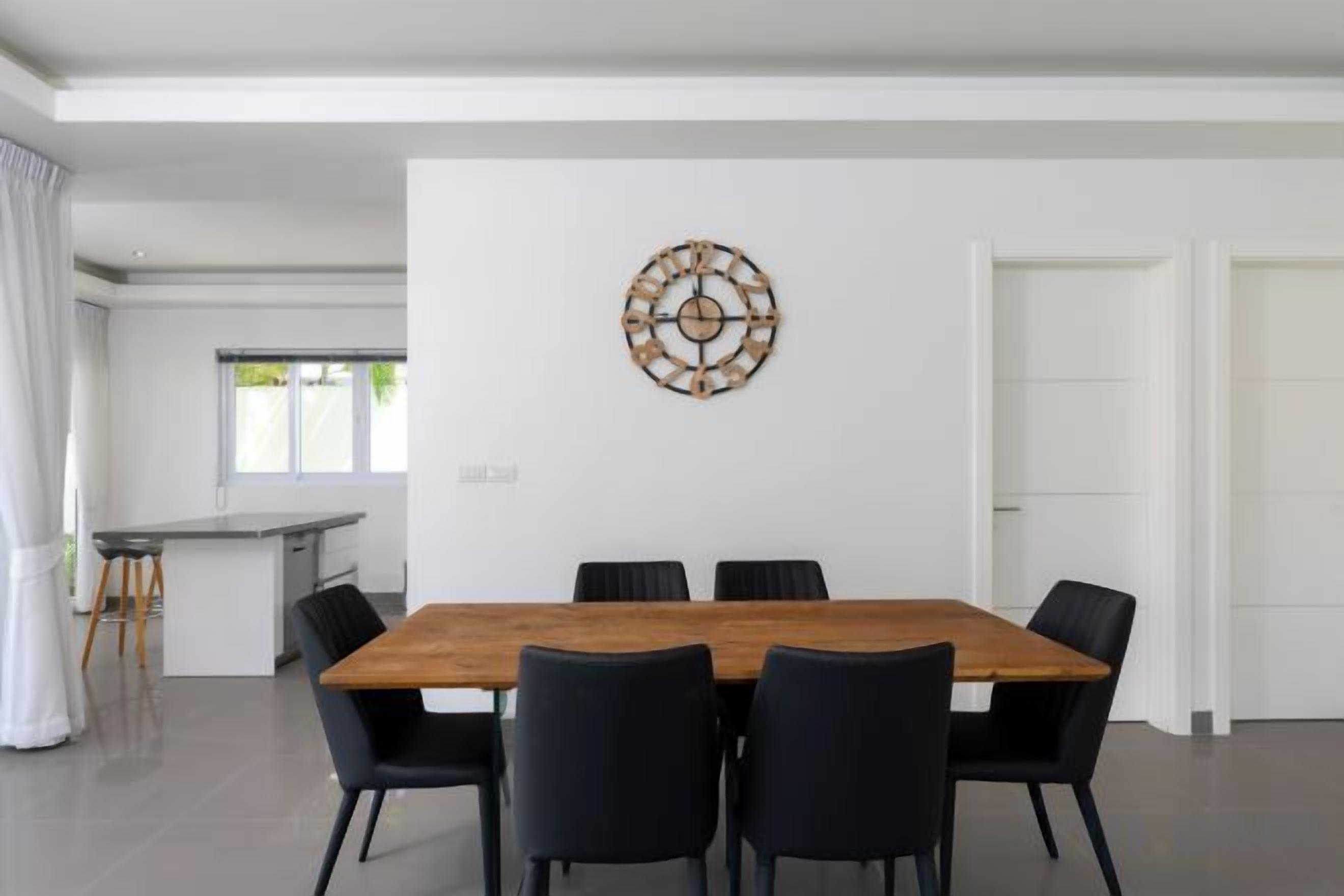 A modern dining area with a wooden table and black chairs, a decorative wall piece, and a view of a kitchen and dining area.