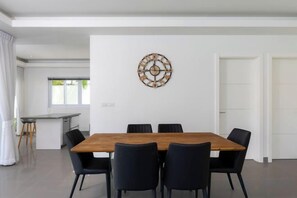 Un espace repas moderne avec une table en bois et des chaises noires, un élément décoratif mural et une vue sur la cuisine et la salle à manger.