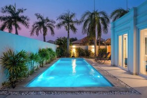 Une piscine à l’eau d’un bleu cristallin, entourée d’un petit muret blanc et de palmiers.