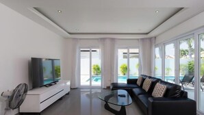 Un salon moderne doté d’un téléviseur à écran plat, d’une table basse en verre, d’un canapé en cuir noir et offrant une vue sur la piscine grâce à de grandes fenêtres.