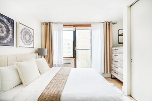 A bedroom with a bed, a nightstand, a lamp, a dresser, and a window with curtains. - 75-3C Duplex 3BR W/D in the unit (New York)