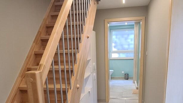 Un interior moderno con una escalera de madera, suelo de baldosas y vista a un baño por una puerta.