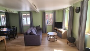 Una sala de estar con sofá, una mesa de comedor, sillas, un televisor y una mesita.