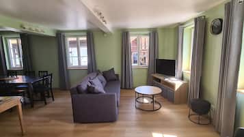 Een woonkamer met een bank, een eettafel, stoelen, een televisie en een bijzettafeltje.
