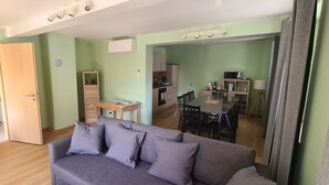 Una sala de estar con sofá gris, escalera de madera y un comedor con mesa y sillas.