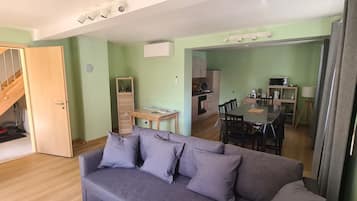 Een woonkamer met een grijze bank, een houten trap en een eethoek met een tafel en stoelen.