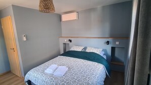 Una cama bien hecha con un edredón y almohadas estampadas, cabecera de madera, unidad de aire acondicionado de pared y una puerta a la izquierda.