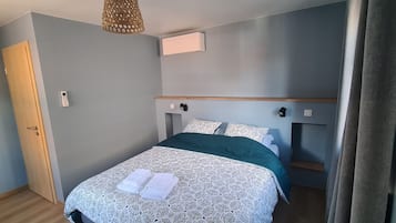 Een net opgemaakt bed met een bedspreide en kussens met een patroon, een houten hoofdbord, een wandairco en een deur aan de linkerkant.