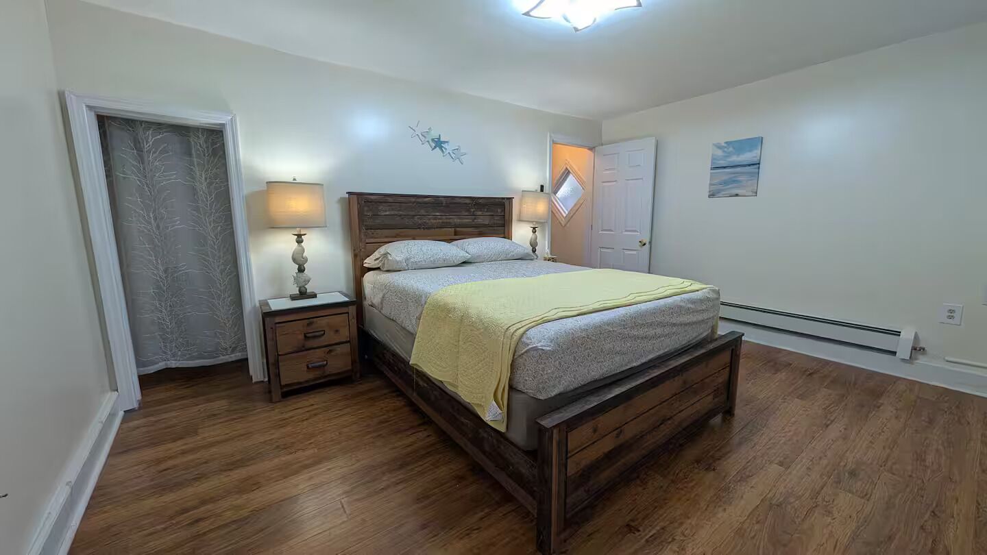 A bedroom with a wooden bed, bedside tables, a nightstand, a door, and a wall with a decorative piece.