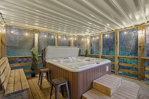 Une terrasse en bois avec un jacuzzi, des bancs en bois et une vue sur la forêt.