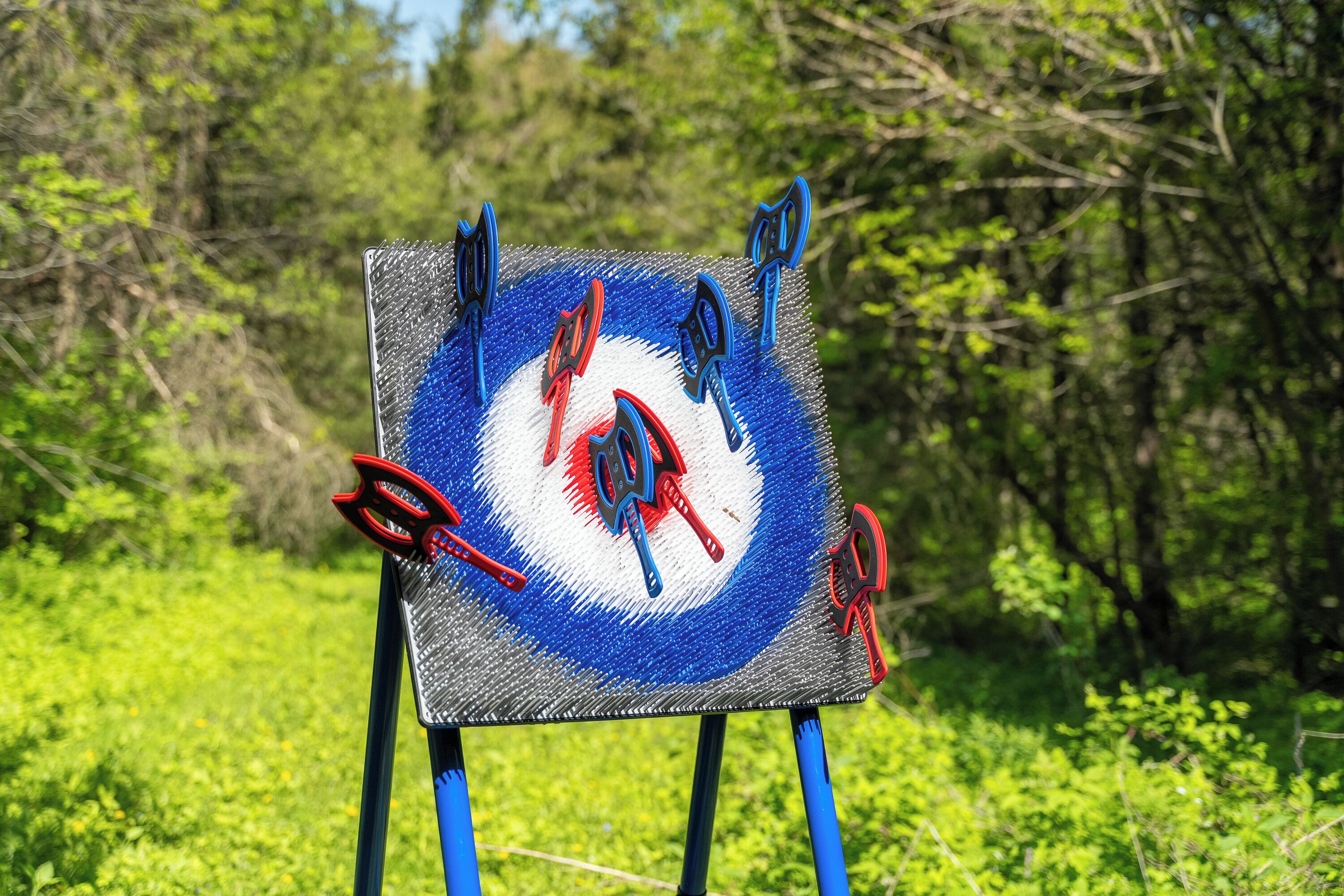 Una pintura cuadrada sobre caballete con diseños abstractos, frente a un paisaje natural.