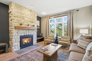 Un salon avec une cheminée en pierre, un canapé, une table basse et une fenêtre avec des rideaux.