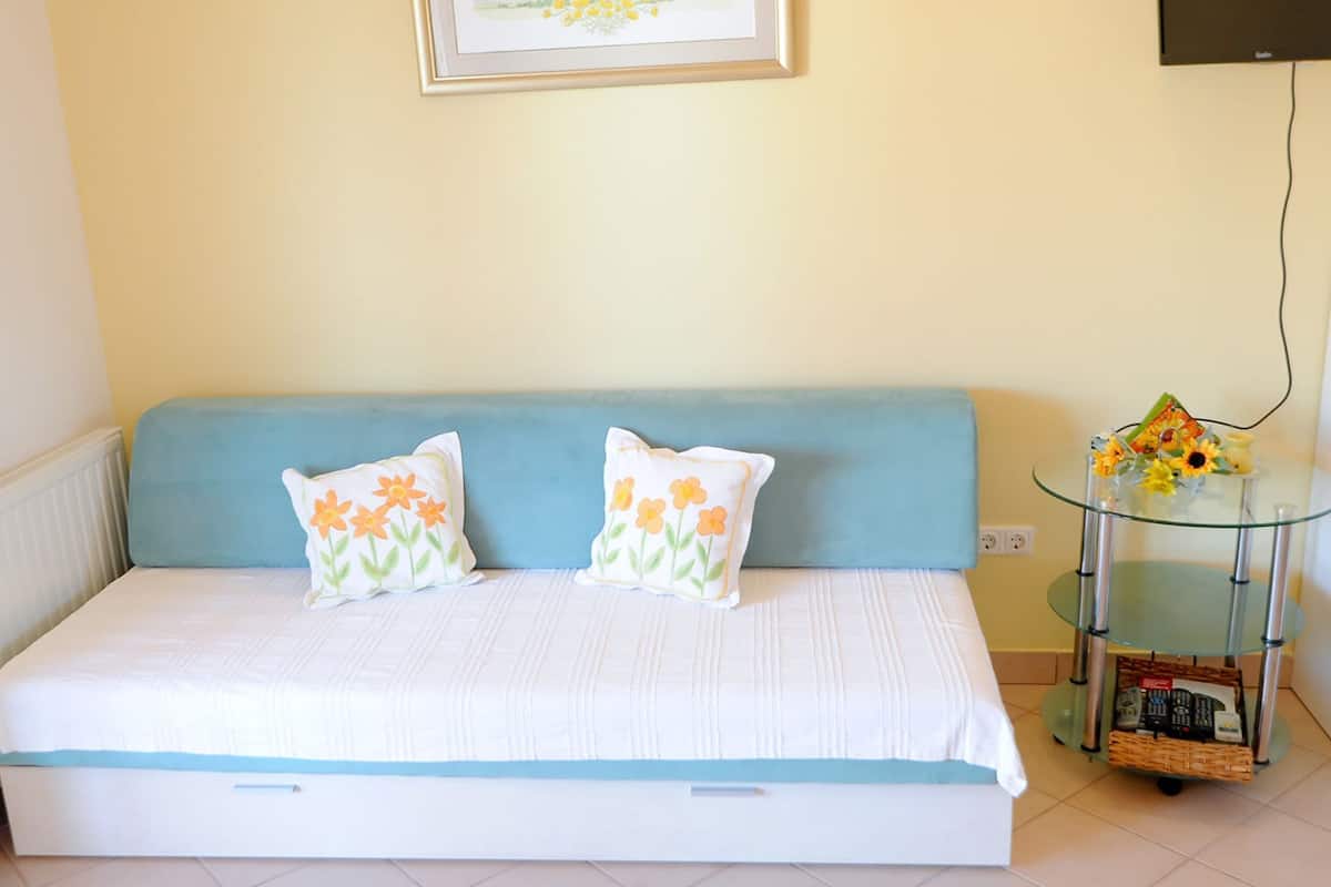 A small, neatly made bed with a blue headboard and two pillows with floral designs. A framed picture hangs on the wall above the bed.