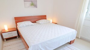 Ein ordentlich bezogenes Bett mit weißer Bettwäsche und zwei Kissen, begleitet von Holzbeistelltischen mit Lampen, in einem Zimmer mit schlichtem, klarem Design.