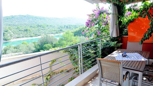 Ein Balkon mit Tisch und Stühlen mit Blick auf einen Fluss und viel Grün.