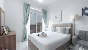 Hotelkamer met een groot bed, nachtkastje, stoel, lamp en raam met gordijnen.